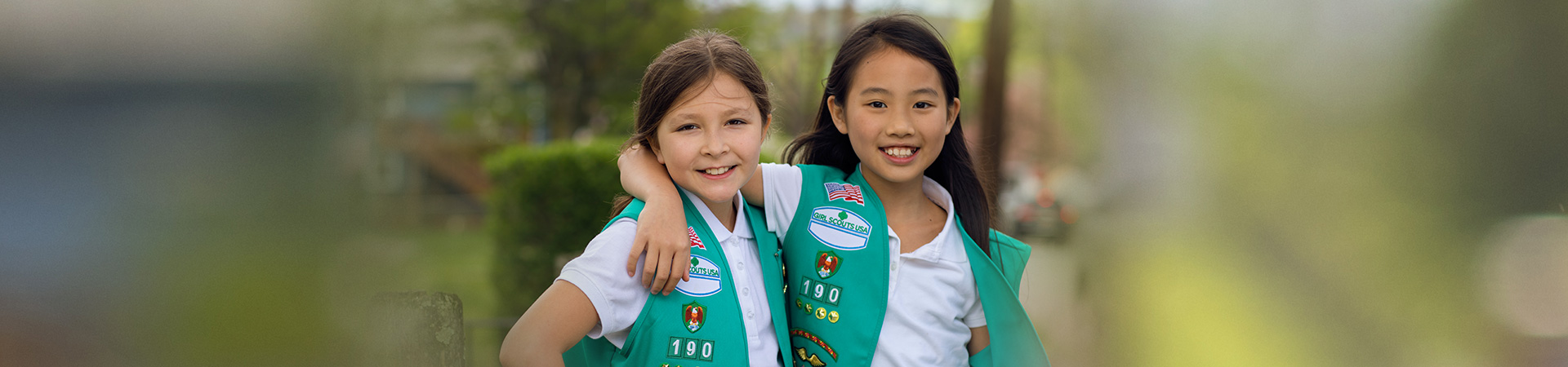  two girl scout juniors outside wearing junior vest uniform smiling 